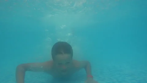 Small boy diving in the pool, touching the floor and looking at the camera Video stock 152692585