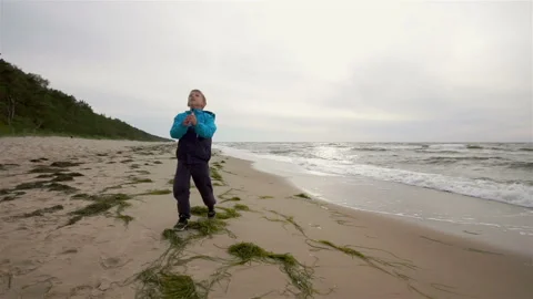 A small boy is flying kites over the sea. It is cold and windy summer. The boy i Vídeos de archivo 87999553