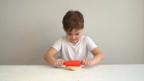Small boy holds rolling pin and rolls dough on white table on kitchen. Stock Footage 128827095