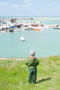 Small boy in jacket and hat looks at the sea pier in the spring Foto stock