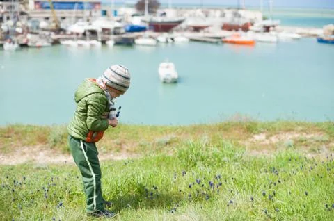 Small boy in jacket, scarf and hat picking flowers Muscari on green slope in  스톡 사진