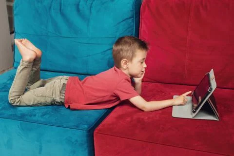 Small boy is lying on the sofa and surfing on tablet Stock Photos