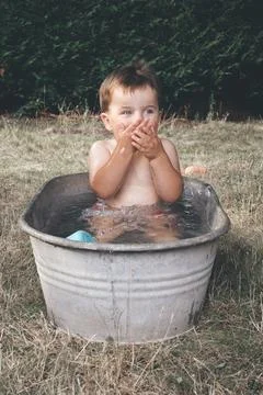 Small boy playing and bathing in retro metal bathtub during hot day Stock Photos