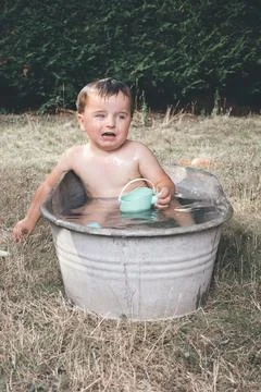 Small boy playing and bathing in retro metal bathtub during hot day Stock Photos