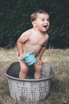 Small boy playing and bathing in retro metal bathtub during hot day Stock Photos