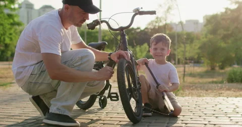 Small boy plays with pump while man checks wheel of bicycle Stockbeeldmateriaal 316763554