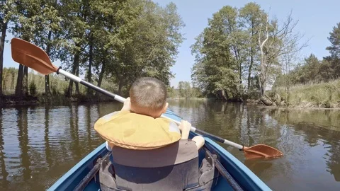 Small boy rowing kayak on shallow river paddling ahead Vídeo Stock 123684092