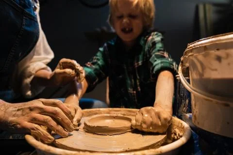 A small boy sculpts a plate out of clay under the supervision of a teacher in a Stock Photos