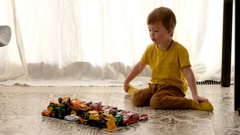 Small boy sits on floor and looks at automobile models Stock Footage 140420391