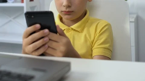 Small boy sitting in front of laptop, watching video on smartphone, addiction Stock-Footage 119035762
