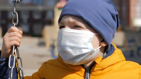 Small boy sitting outside on a swing during a pandemic wearing fabric facemask Video stock 127758727
