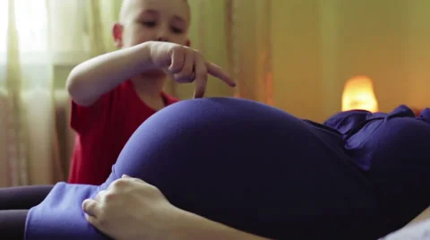 A small boy stomping with his fingers on mother's belly, as if making steps. Stock Footage 63237191
