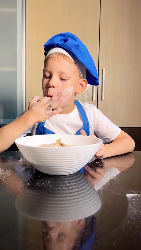 Small boy is tasting raw dough. Son is helping mother to prepare dough for ba Stock Footage 295192764