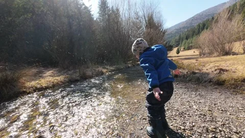 Small boy throwing a stone into a stream causing a water splash Stock Footage 305275541