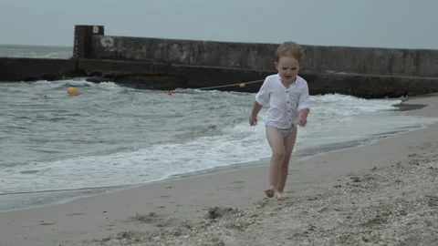 A small boy trunks is happy to run along the sandy beach along the water Stock Footage 246083068