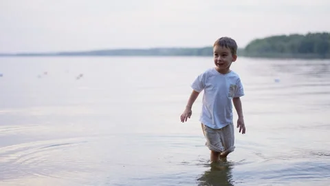 Small boy wading in calm lake water at sunset. Side view of toddler stepping Stock Footage 336383080
