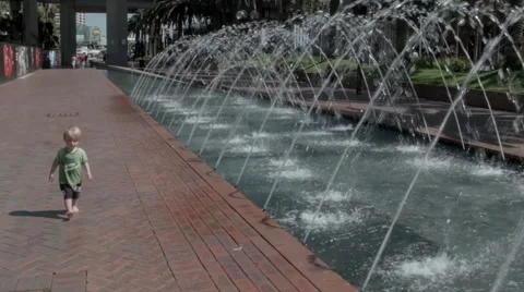 Small boy walking past a water fountain feature 2 Stock Footage 59130854