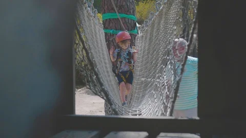 Small boy walks along a rope bridge in helmet and climbing gear Stock Footage 88903686
