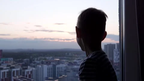 Small boy watching cityscape from high rise window at sunset Stock Footage 312168494
