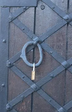 Small brass padlock locking a medieval style wooden gate with iron reinforc.. Stock Photos