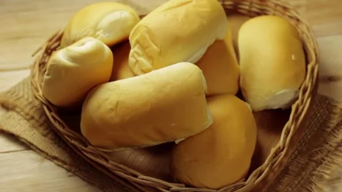 Small bread rolls arranged in a wicker basket on a rustic wooden table. Видео 337081155
