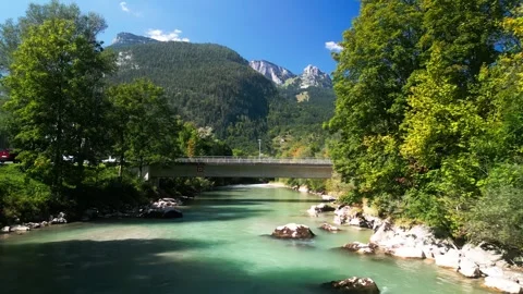 Small bridge over shallow mountain river with trees around on blue sky day Stock Footage 250084394