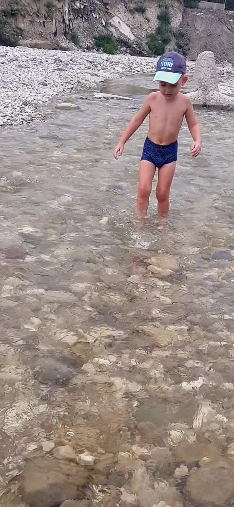 A small bright boy in a cap walks along the river in summer Stock Footage 240081292