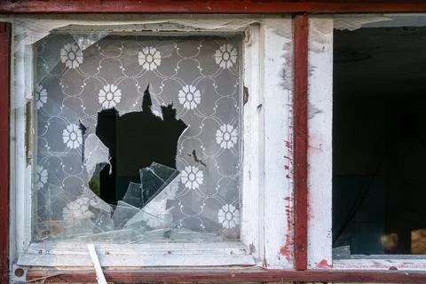 Small broken window with red frame and window shades torn apart. Detail of an Stock Photos