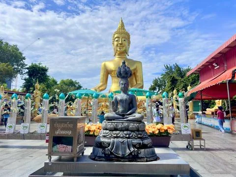 Small bronze Buddha statue in front of giant golden Buddha at Wat Phra Yai Stock Photos