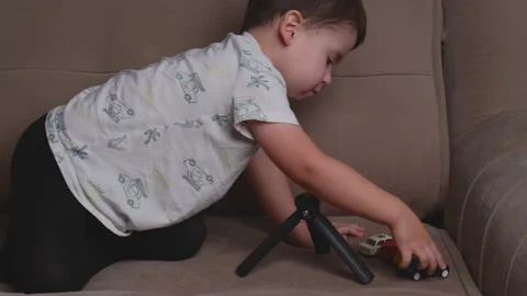 Small brunette boy is playing with plastic cars on the couch moving them and Stock Footage 146512983