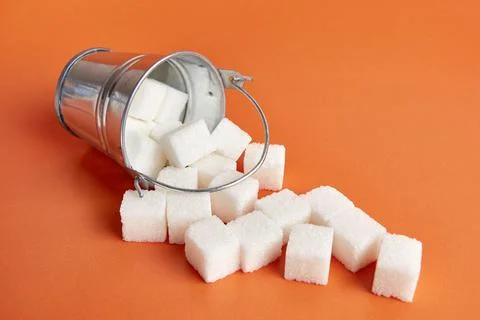 A small bucket with cubes of pressed sugar on an orange background. Stock Photos