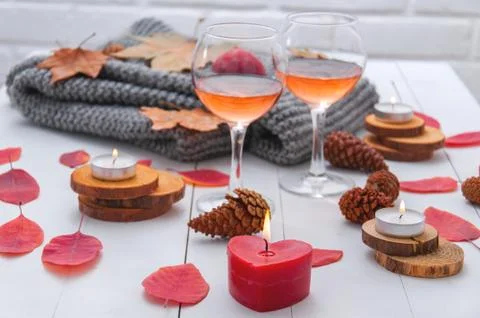 Small burning candles, two glasses with rose wine, cones, dry red leaves, a g Stock Photos