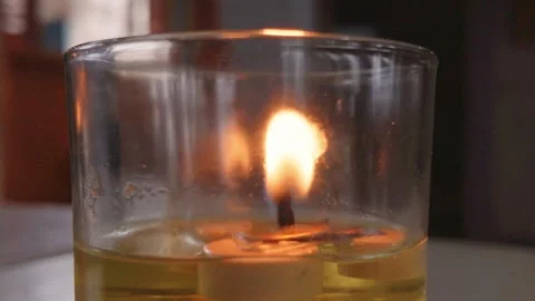 A small burning oil lamp inside a clear glass container on a table. Video stock 343402914
