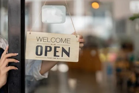 Small business owner smiling while turning the sign for the opening of the place Stock Photos