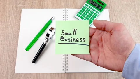 Small business text on a sheet of notes in the hands of a businessman at a desk Stock Footage 279693850