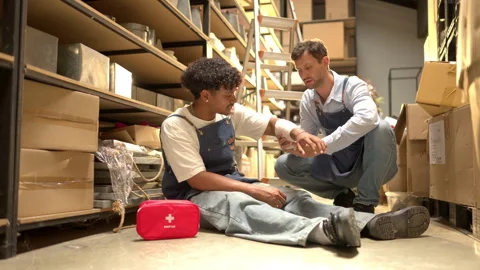 Small business workers handling a minor injury in a storage warehouse Stock Footage 339643136