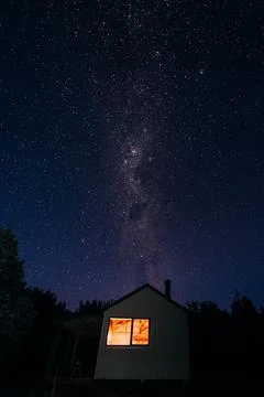 A small cabin sits beneath a vast night sky filled with twinkling stars Stock Photos
