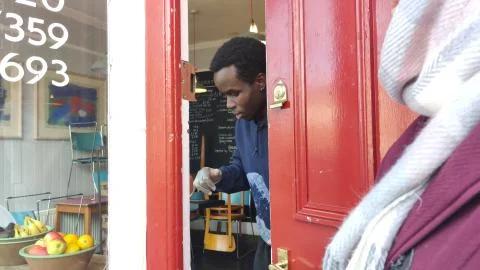 SMALL CAFE SERVES COFFEE THROUGH CRACK IN DOOR DURING COVID-19 PANDEMIC Stock Photos