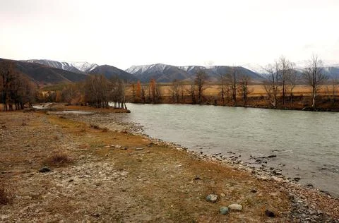 A small calm river flowing through the autumn steppe at the foot of high moun Stock Photos