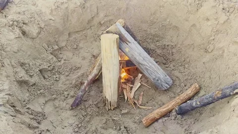 Small campfire burning between wooden logs in a sandy fire pit Stock Footage 345602962