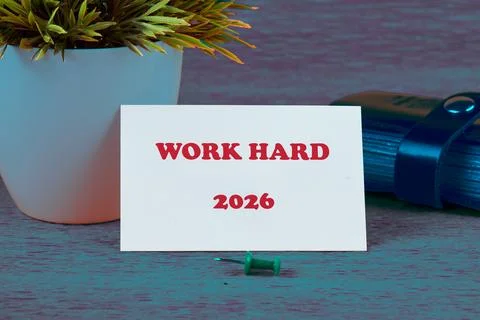 A small card saying Work Hard sits by a green pushpin and stylish notebook Foto stock