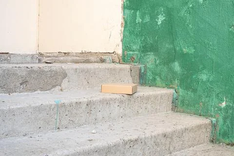 Small cardboard package left on concrete steps near building entrance Stock Photos