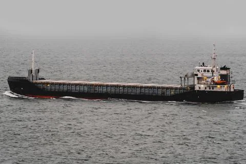 Small cargo ship sailing through dense fog at sea. Stock Photos