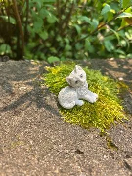 Small cat figurine resting on moss in a garden setting Stockfoto's