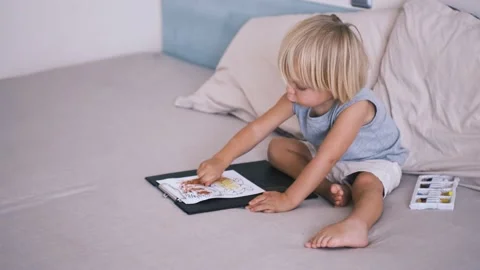 A small caucasian boy in a gray T-shirt and shorts on the bed draws with colored Stock Footage 220731805