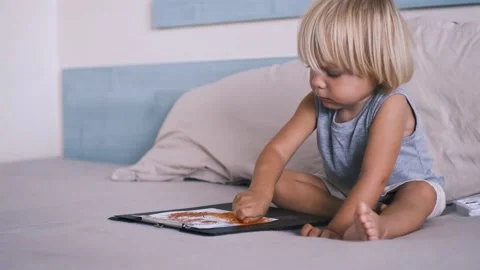 A small caucasian boy in a gray T-shirt and shorts on the bed draws with colored Stock Footage 220732224
