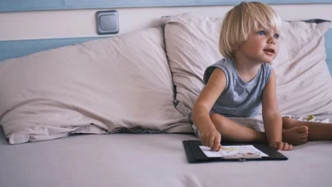 A small caucasian boy in a gray T-shirt and shorts on the bed draws with colored Stock Footage 220732286