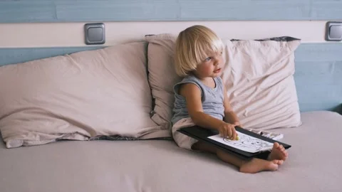 A small caucasian boy in a gray T-shirt and shorts on the bed draws with colored Stock Footage 220732339