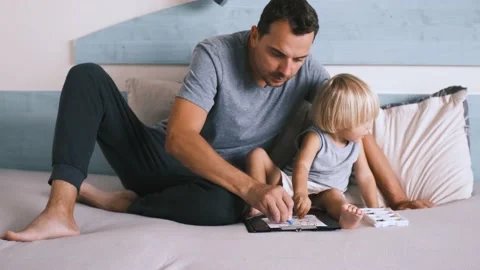 A small caucasian boy with his father on the bed draw with colored pencils. Stock Footage 220731982