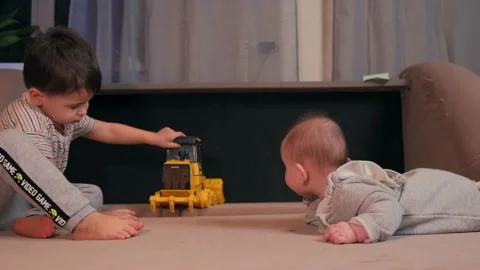 Small caucasian boy is playing on the couch with a plastic toy car while newborn Stock Footage 150857966